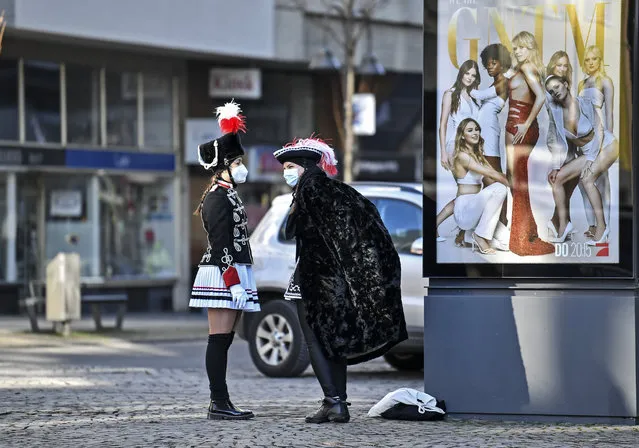 Two women in costumes stand beside an advertising for “Germany's next top model” TV show at the “Alter Markt” where normally tens of thousands of revelers dressed in carnival costumes would celebrate the start of the street carnival in Cologne, Germany, Thursday, February 11, 2021. This year all carnival celebrations are banned due to the coronavirus pandemic. (Photo by Martin Meissner/AP Photo)