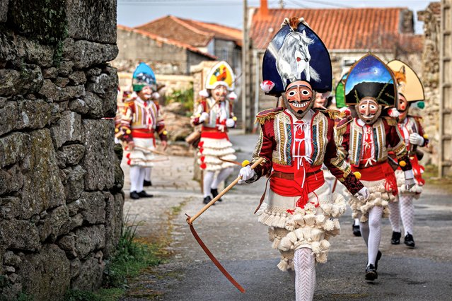 Locals dress up as Mazcaras to celebrate Entroido on February 21, 2023 in A Xironda, Spain. Entroido is an ancient rural carnival celebrated in Galicia during the previous days of Ash Wednesday. Each town has its traditional characters and costumes. In the small village of A Xironda, locals dress up as Mazcaras with their characteristic masks, cowbells at the waist and whips, and then run through the streets. (Photo by Brais Seara Fernandez/Getty Images)