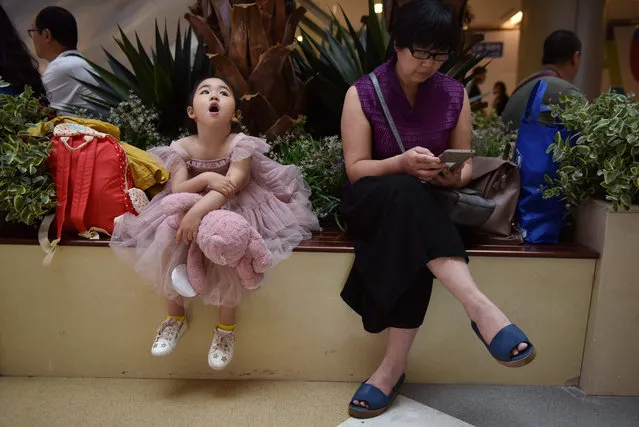 This photo taken on May 26, 2019 shows a child model waiting with a relative before taking the stage at a child model contest in Beijing. Manicured children strut down the catwalk at a Beijing fashion show, one of thousands of events driving huge demand for child models in China that insiders warn leaves minors vulnerable to physical abuse, 12-hour-days and unrelenting pressure from pushy parents. (Photo by Greg Baker/AFP Photo)