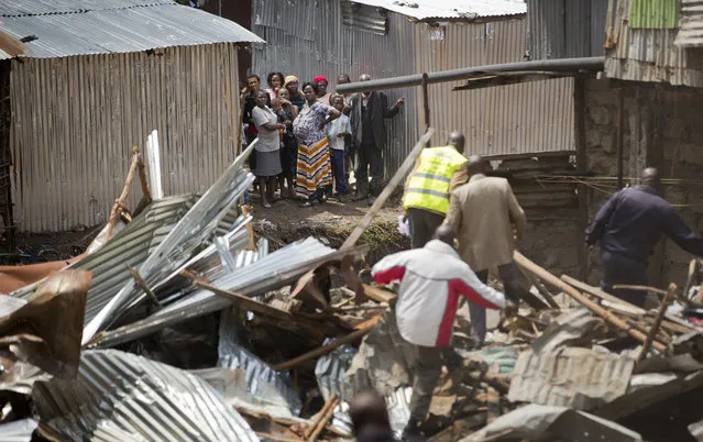 Residents look across after a mechanical digger demolished their neighbors' shacks on the other side of the river, close to the site of last week's building collapse, after their homes were deemed unfit for habitation, in the Huruma neighborhood of Nairobi, Kenya Friday, May 6, 2016. (Photo by Ben Curtis/AP Photo)