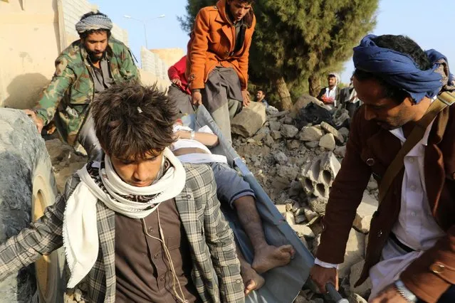 Rescuers carry a man injured by air strikes on a detention center in Saada, Yemen on January 21, 2022. (Photo by Naif Rahma/Reuters)