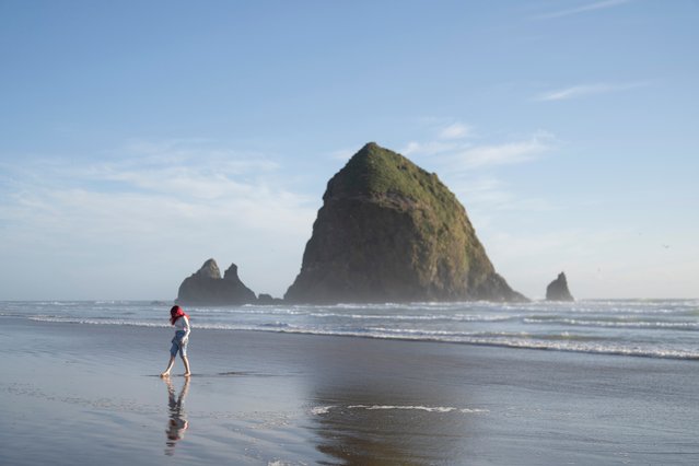 With Haystack Rock in the background, Julie Amschler, of Springfield, Mo., walks along the beach on Thursday, June 13, 2024, in Cannon Beach, Ore. (Photo by Jenny Kane/AP Photo)