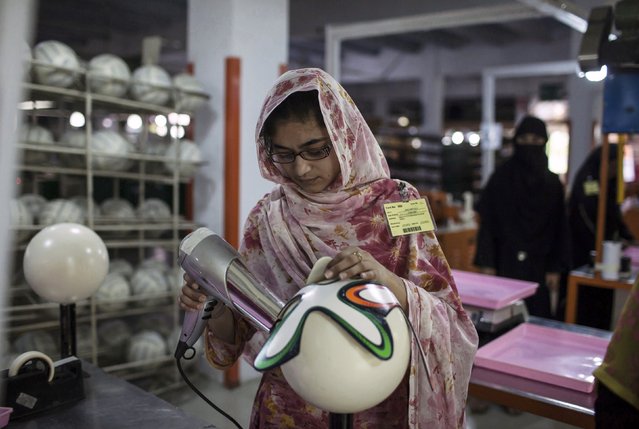 An employee uses hot air as she sticks outer panels on a soccer ball inside the soccer ball factory that produces official match balls for the 2014 World Cup in Brazil, in Sialkot, Punjab province May 16, 2014. (Photo by Sara Farid/Reuters)