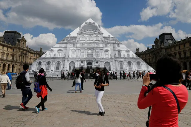 Tourists walk near French artist JR's latest work, an image of the facade of Paris' Louvre that covers the museum's Pyramid entrance in Paris, France, May 25, 2016. (Photo by Pascal Rossignol/Reuters)