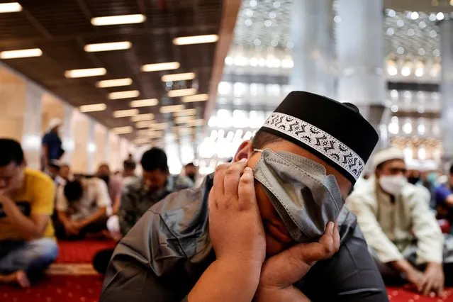 A Muslim boy covers his face with a protective mask as he falls asleep while attending the first Friday prayers during the holy fasting month of Ramadan at the Grand Istiqlal Mosque in Jakarta, Indonesia on April 8, 2022. (Photo by Willy Kurniawan/Reuters)