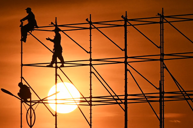 Workers stand on scafolding at sunset in Hanoi on September 4, 2024.  (Photo by Nhac Nguyen/AFP Photo)