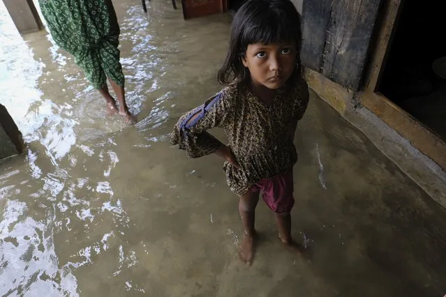 A girl reacts to camera as he family members inspect their damaged belongings at her home as flood water levels recede slowly in Sylhet, Bangladesh, Wednesday, June 22, 2022. (Photo by Mahmud Hossain Opu/AP Photo)