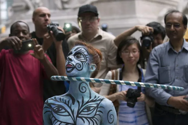 A model hula hoops after being painted as spectators stand near at Columbus Circle as body-painting artists gathered to decorate nude models as part of an event featuring artist Andy Golub, Saturday, July 26, 2014, in New York. Golub says New York was the only city in the country that would allow his inaugural Bodypainting Day. (Photo by John Minchillo/AP Photo)