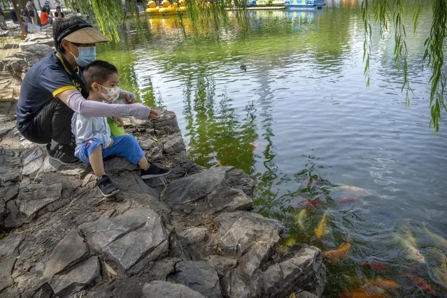 A woman and boy wearing face masks feed fish in a pond at a public park in Beijing, Friday, July 8, 2022. (Photo by Mark Schiefelbein/AP Photo)