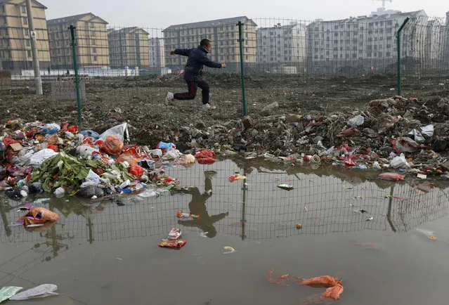 A child is reflected in a drainage ditch as he jumps over trash at a village which will soon be demolished, on the outskirts of Jiaxing city, Zhejiang province, January 12, 2013. New residential buildings are seen in the background. (Photo by William Hong/Reuters)