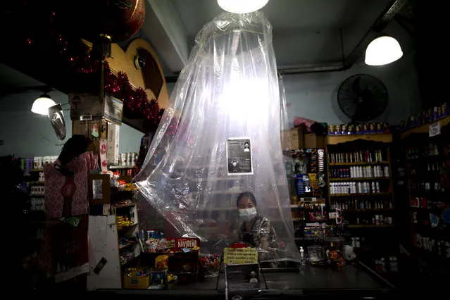 A supermarket cashier waits for costumers behind a makeshift plastic curtain as a precaution against the spread of the new coronavirus, in Buenos Aires, Argentina, Monday, March 16, 2020. (Photo by Natacha Pisarenko/AP Photo)