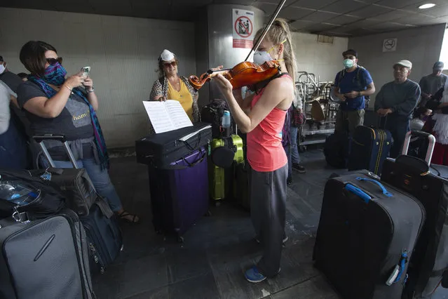 A traveler plays her violin prior to getting on a charter flight coordinated by the U.S. embassy at La Aurora airport in Guatemala City, Monday, March 23, 2020. American citizens stranded abroad because of the coronavirus pandemic are seeking help in returning to the United States. (Photo by Moises Castillo/AP Photo)