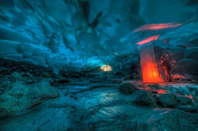 A friend of Ron Gile holding up a red road flare inside the amazing Alaskan ice cave. (Photo by Ron Gile/Caters News)