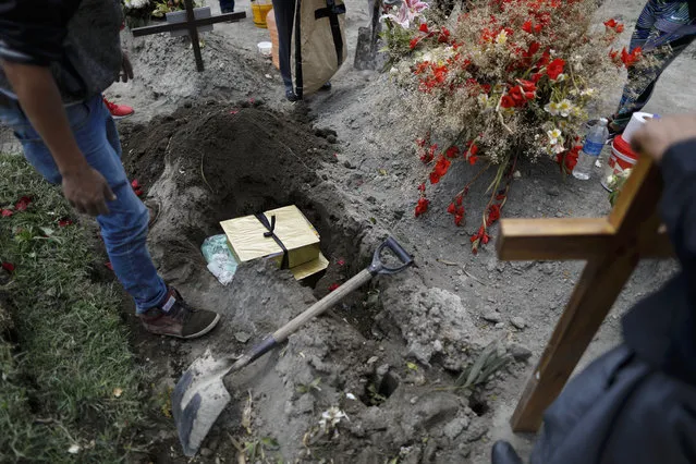 Boxes containing the flowers, lime and other symbolic elements used in the cross-raising ceremony are buried atop the grave of Luz Maria Gonzalez, as her family marks nine days since her burial, in the Municipal Cemetery of Valle de Chalco on the outskirts of Mexico City, Saturday, July 4, 2020. Maria Luz Gonzalez, 56, who had long suffered from asthma, diabetes and hypertension, died two days after her son, who was hospitalized for breathing problems and a cough before dying of complications said to be related to pneumonia and undiagnosed diabetes. (Photo by Rebecca Blackwell/AP Photo)