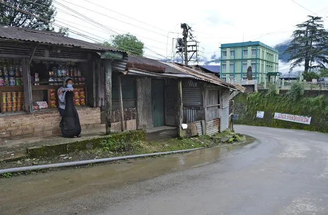 A Naga wearing a face mask leans on a guitar and sits by a deserted road in Kohima, capital of the northeastern Indian state of Nagaland, Thursday, August 13, 2020. India has the third-highest caseload after the United States and Brazil, but only the fifth-highest death toll, and authorities say the fatality rate has dropped below 2% for the first time. (Photo by Yirmiyan Arthur/AP Photo)