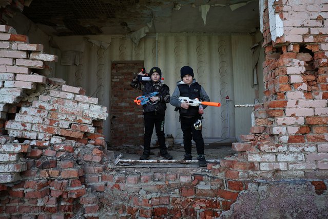 Brothers Andrii, 8, and Maksym Tupkalenko, 6, two of the last children left in their frontline village, pose for a photo with toy guns, their favorite toys, in Kalynove, Kharkiv region, Ukraine, on April 11, 2025. Instead of scampering across playgrounds, the brothers climb through abandoned trenches and charred shells of armoured vehicles that sit on the outskirts of the village, playing soldiers and setting up make-believe checkpoints to vet fellow villagers. “They're kids afflicted by war”, said their mother Varvara Tupkalenko, 30. (Photo by Violeta Santos Moura/Reuters)