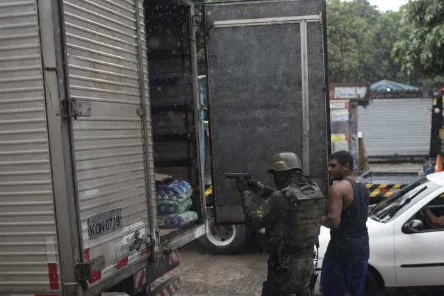 In this Friday, February 23, 2018 photo, a soldier takes position as a driver opens the back of his trailer during a spot inspection at a checkpoint at the Vila Kennedy slum in Rio de Janeiro, Brazil. Similar to previous troop deployments in Rio, soldiers have had a secondary role, setting up checkpoints and perimeters but not leading attempts to arrest armed traffickers. (Photo by Leo Correa/AP Photo)