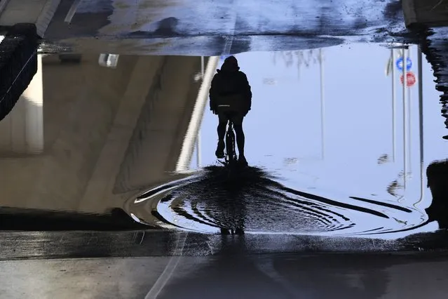A man rides a bicycle through a puddle under a bridge in Belgrade, Serbia, Wednesday, February 15, 2023. (Photo by Darko Vojinovic/AP Photo)