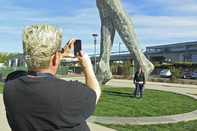 In this photo taken Wednesday October 19, 2016, art teachers Jo Sutton, left, and Jennifer Jervis, right, take pictures beneath a 55-foot nude statue in San Leandro, Calif. The statue of a naked woman is stirring controversy and a lot of conversation. City officials and the sculptor of the steel nude, which was unveiled this week across from San Leandro's main commuter train stop, say they want to draw attention to “feminine energy”. Critics say the 13,000-pound towering nude is not appropriate public art. (Photo by Jocelyn Gecker/AP Photo)