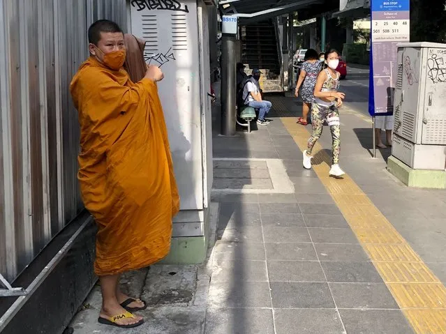 A Buddhist monk wearing a face covering to help prevent the spread of coronavirus waits for a bus along Sukhumvit Road in Bangkok on Wednesday, December 23, 2020. Thailand has kept the coronavirus largely in check for most of the year but is facing a challenge from a large outbreak of the virus among migrant workers in a province close to the Thai capital. (Photo by Adam Schreck/AP Photo)