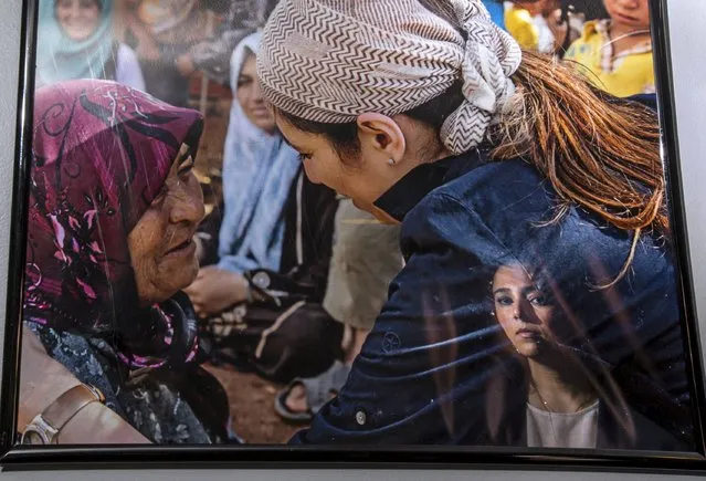 Lina Sergie Attar is reflected in a photograph of her visit to a Syrian refugee camp, that hangs on her wall at her home in Lake Forest, Illinois, October 25, 2015. (Photo by Jim Young/Reuters)