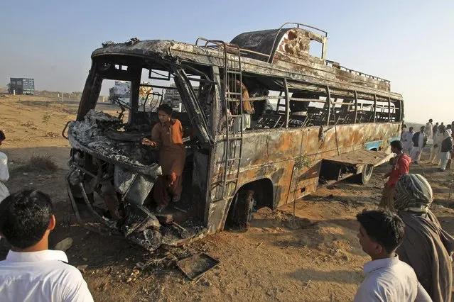 Pakistani gather around and inside the wreckage of a passenger bus that was destroyed after colliding with an oil tanker on a highway about 50 kilometers (31 miles) outside of Karachi, Pakistan, Sunday, January 11, 2015. More than 50 people were killed in the accident. (Photo by Fareed Khan/AP Photo)