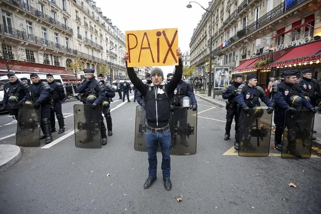 A man holds a placard which reads "Peace" in front of CRS riot policemen near the Place de la Republique after the cancellation of a planned climate march following shootings in the French capital, ahead of the World Climate Change Conference 2015 (COP21), in Paris, France, November 29, 2015. (Photo by Eric Gaillard/Reuters)