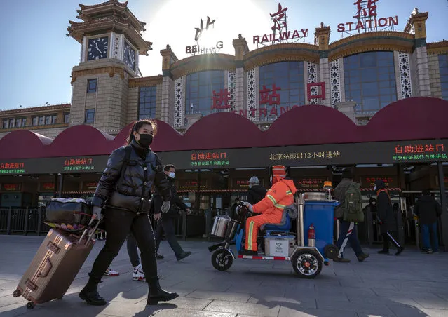 Travelers wearing face masks to protect against the spread of the coronavirus walk with their luggage at the Beijing Railway Station in Beijing, Thursday, January 28, 2021. (Photo by Mark Schiefelbein/AP Photo)