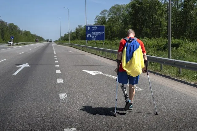 Ukrainian war veteran Oleksandr Shvetsov carries a Ukrainian flag as he walks along a highway towards Kyiv from Zhytomyr to meet his friend Serhii Khrapko ahead of their 120-kilometer (75 mile) walk to raise money for medical equipment in honor of their comrades wounded in Russia's war against their homeland in Stavyshche village, Zhytomyr region, Ukraine, on Thursday, May 18, 2023. They raised 3.1 million hryvnias ($84,000), short just the 500,000 hryvnias ($14,000) needed to purchase a new gastroscope for Ukraine's National Military Medical Clinical Center. (Photo by Roman Hrytsyna/AP Photo)