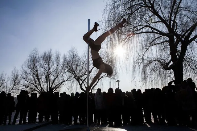 People watch a woman perform a pole dance in subzero temperature at a park in Changchun, Jilin province, January 19, 2015. (Photo by Reuters/Stringer)