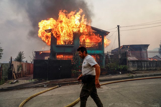 A person walks in front of a burning building as fire and smoke rise from a forest fire in the Biobio region where, according to local media, multiple wildfires prompted emergency evacuations, in Concepcion, Chile, January 18, 2026. (Photo by Juan Gonzalez/Reuters)