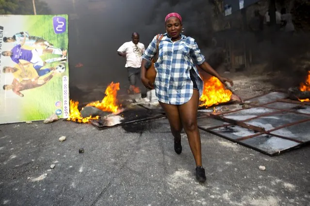 People run past a barricade set up and burned during a protest over the cost of fuel in Port-au-Prince, Haiti, Friday, July 6, 2018. Major protests erupted Friday in Haiti as the government announced a sharp increase in gasoline prices, with demonstrators using burning tires and barricades to block major streets across the capital and in the northern city of Cap-Haitien. (Photo by Dieu Nalio Chery/AP Photo)