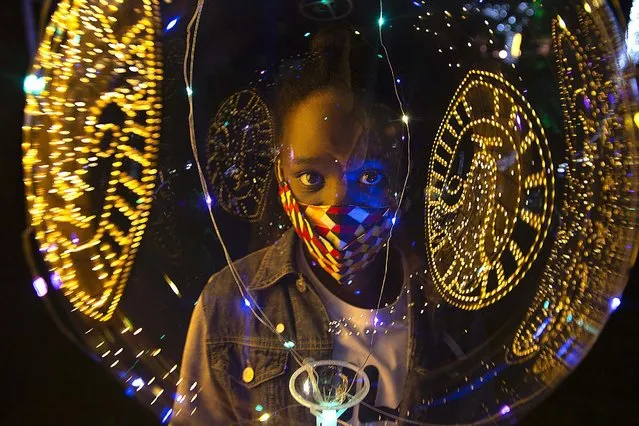 Christmas lights are reflected on a ballon as a child wears a face mask to protect against coronavirus at the Johannesburg Zoo's Festival of Lights Tuesday December 1, 2020. (Photo by Denis Farrell/AP Photo)