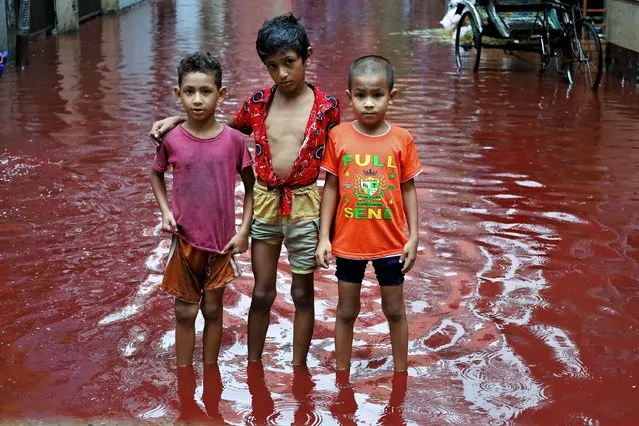 Three boys stand in a street flooded from heavy rain mixed with the blood of animals slaughtered for Eid Ul Adha in Dhaka on June 29, 2023. (Photo by Syed Mahabubul Kader/ZUMA Press Wire/Rex Features/Shutterstock)
