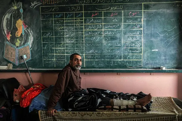 Injured Palestinian Akram Al-Zein, 49, sits under a school chalkboard at the Ras Al-Naqoura school in Khan Yunis, in the southern Gaza Strip, after being transferred from the Indonesian Hospital in the north, on November 22, 2023, amid the ongoing battles between Israel and the Palestinian militant group Hamas. (Photo by Said Khatib/AFP Photo)