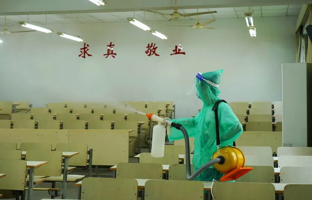 A worker wearing protective suit sprays disinfectant inside a classroom of Zhejiang A&F University before the new semester on August 22, 2021 in Hangzhou, Zhejiang Province of China. (Photo by Chen Shengwei/VCG via Getty Images)