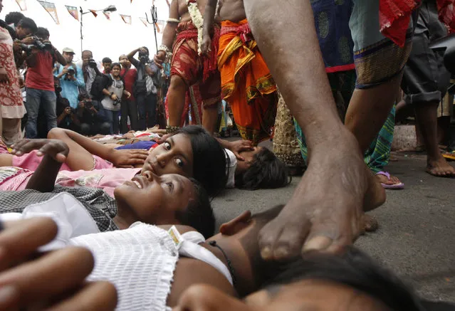 A girl watches as a Hindu holy man (not pictured) touches a child with his foot as part of a ritual to bless him during the Gajan festival in Kolkata April 13, 2015. Hundreds of faithful devotees offer sacrifices and perform acts of devotion during the festival in the hopes of winning the favour of Hindu god Shiva and ensuring the fulfillment of their wishes, and also to mark the end of the Bengali calendar year. (Photo by Rupak De Chowdhuri/Reuters)