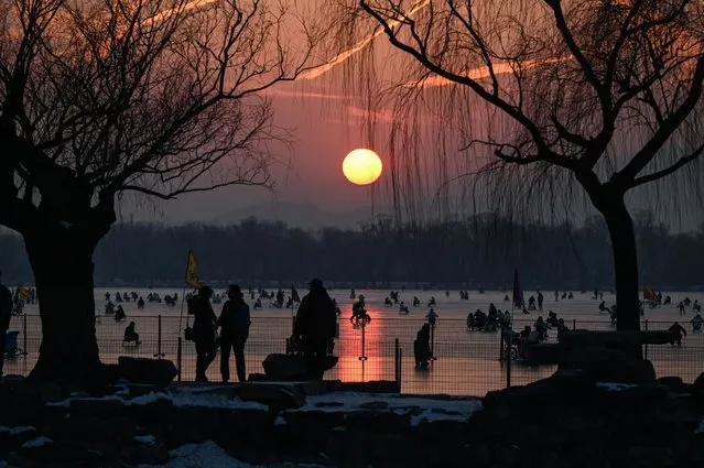 People ride sleds on a frozen lake at the Summer Palace during sunset in Beijing on December 28, 2023. (Photo by Jade Gao/AFP Photo)