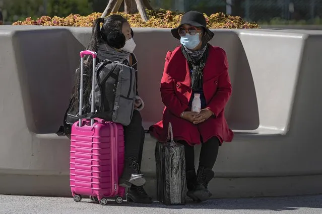 Women wearing face masks to help curb the spread of the coronavirus chat each other on a bench outside a shopping mall in Beijing, Thursday, October 21, 2021. (Photo by Andy Wong/AP Photo)