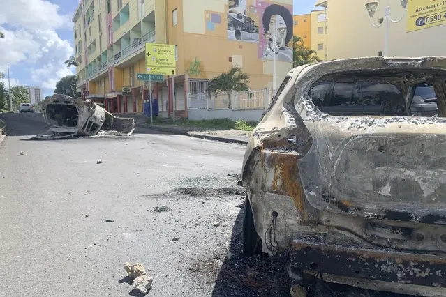Charred car are pictured in a s street of Le Gosier, Guadeloupe island, Sunday, November 21, 2021. French authorities sent police special forces to the Caribbean island of Guadeloupe, an overseas territory of France, as protests over COVID-19 restrictions erupted into rioting and looting for the third day in a row. On Sunday, many road blockades by protesters made traveling across the island nearly impossible. (Photo by Elodie Soupama/AP Photo)