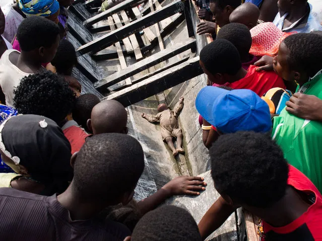 People watch the body of a child retrieved by the Ugandan Police divers on Lake Albert near Kitebere on March 23, 2013. As many as 60 people are feared to have drowned when a boat capsized on Lake Albert on the border between Uganda and Democratic Republic of Congo, reports said on March 22. (Photo by Michele Sibiloni/AFP Photo)