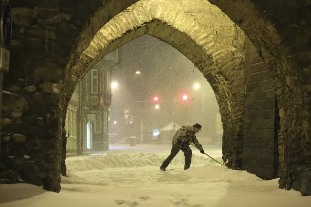 A resident shovels snow under an archway in Wernigerode, Germany, early Sunday morning, February 7, 2021. Low Tristan has caused huge amounts of snow in the Harz mountains, like here in Wernigerode. (Photo by Matthias Bein/dpa via AP Photo)