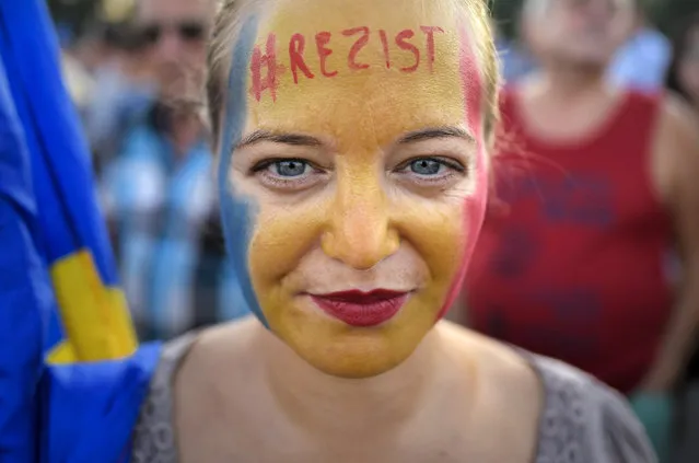 A woman with the Romanian flag colors and the word “Resist” painted on her face takes part in an anti-government protest in Victoria Square, outside the government headquarters in Bucharest, Romania, Saturday, August 10, 2019. Thousands joined a protest, demanding the resignation of the government, one year after a similar rally turned violent and left dozens of participants and members of the riot police injured. (Photo by Andreea Alexandru/AP Photo)