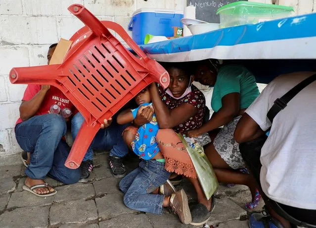 Migrants use a chair to protect themselves from rocks during a protest by migrants to demand speedy processing of humanitarian visas to continue on their way to the United States, outside the office of the National Migration Institute (INM) in Tapachula, Mexico on February 22, 2022. (Photo by Jacob Garcia/Reuters)