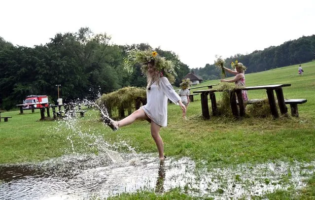 A girl wearing traditional Ukrainian clothes dances in a puddle after heavy rain during the celebrations of the Kupala night in Pyrohiv, near Kiev, on July 6, 2021. During the celebration, an ancient slavic ritual related to the summer solstice, people wear wreaths, jump over fires and bathe naked in rivers and lakes. (Photo by Sergei Supinsky/AFP Photo)