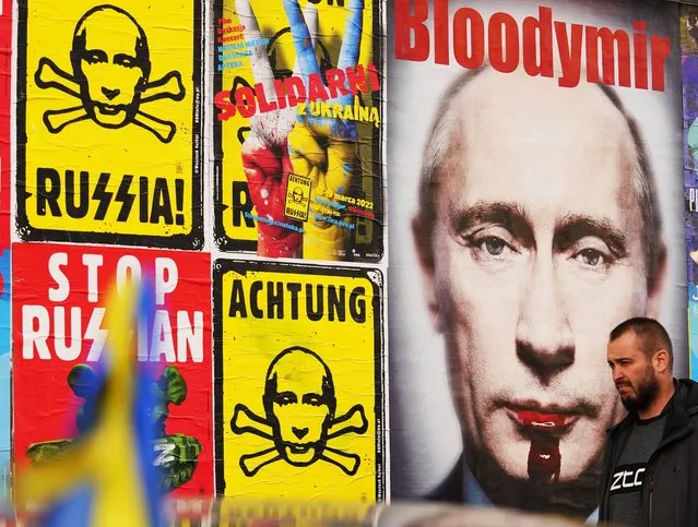A man walks past a wall with posters depicting Russian President Vladimir Putin in Warsaw, Poland, on Thursday, March 24, 2022. Ukraine President Volodymr Zelenskyy called on people worldwide to gather in public Thursday to show support for his embattled country as he prepared to address U.S. President Joe Biden and other NATO leaders gathered in Brussels on the one-month anniversary of the Russian invasion. (Photo by Petr David Josek/AP Photo)