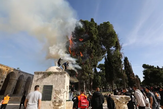 A fire break out in a tree in the courtyard of the Masjid al-Aqsa, as the Israeli police intervene against the Palestinians, who respond to raid, with sound and gas bombs after a morning prayer at Masjid al-Aqsa in East Jerusalem on April 22, 2022. Israeli forces raid with blast bomb and rubber bullets. (Photo by Mostafa Alkharouf/Anadolu Agency via Getty Images)