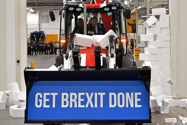 Britain's Prime Minister Boris Johnson drives a JCB through a symbolic wall with the Conservative Party slogan 'Get Brexit Done' in the digger bucket, during an election campaign event at the JCB manufacturing facility in Uttoxeter, England, Tuesday December 10, 2019.  The Conservative Party are campaigning for their Brexit split with Europe ahead of the UK's General Election on Dec. 12. (Photo by Ben Stansall/Pool via AFP Photo)