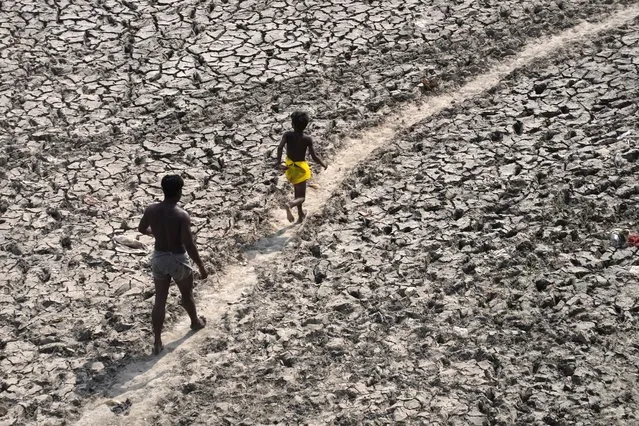 A man and a boy walk across an almost dried up bed of river Yamuna following hot weather in New Delhi, India, Monday, May 2, 2022. An unusually early and brutal heat wave is scorching parts of India, where acute power shortages are affecting millions as demand for electricity surges to record levels. (Photo by Manish Swarup/AP Photo)