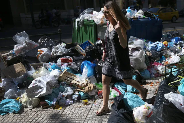A woman is passing by piles of garbage that has formed on pavements in Athens due to the mobilization of workers, on 21 June 2017. About 6,500 contract agents of municipalities working in the cleaning sector are in danger of losing their jobs due to the non-renewal of their employment contracts. (Photo by Orestis Panagiotou/EPA)